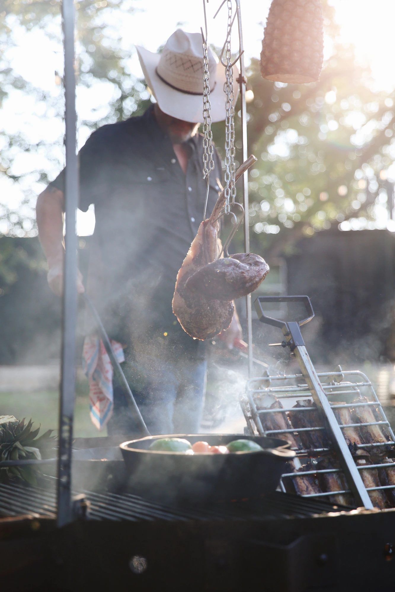 The Rock Raven chef tending hanging cuts in drifting oak smoke at golden hour
